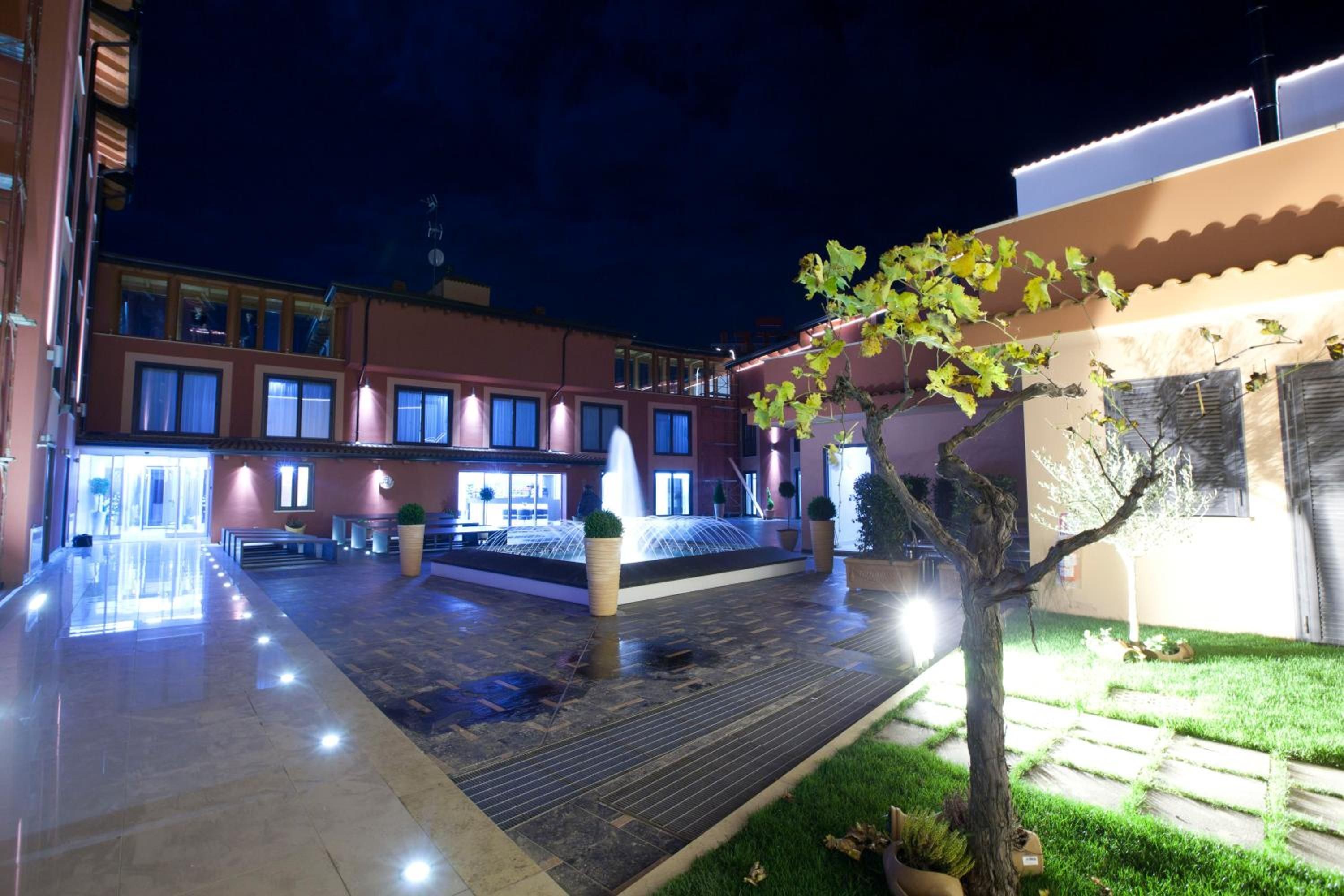 A courtyard with a fountain, potted plants, and a building with multiple windows.