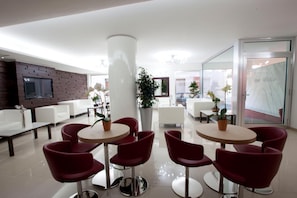 Un hall d’hôtel moderne avec des tables rondes et des chaises rouges, une grande colonne et un téléviseur fixé au mur.