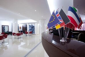 A modern hotel lobby with a reception desk, red chairs, and a glass partition. - Hotel Eridano (Sannazzaro de Burgondi)