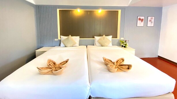 Une chambre d’hôtel avec deux lits, un grand miroir et une petite table sur laquelle se trouve un vase.