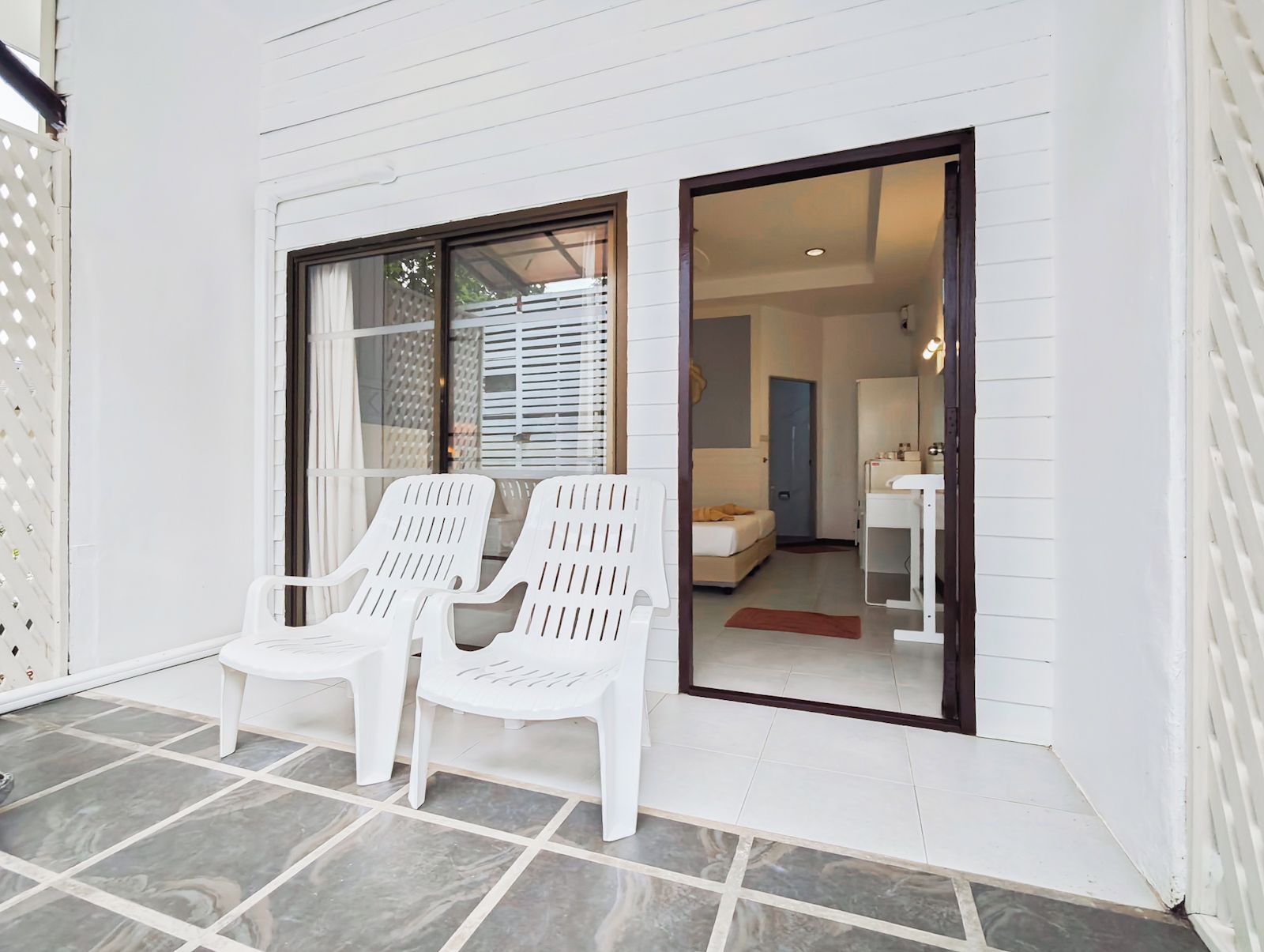 A room with two white plastic chairs, a bed, and a bathroom visible through an open door.