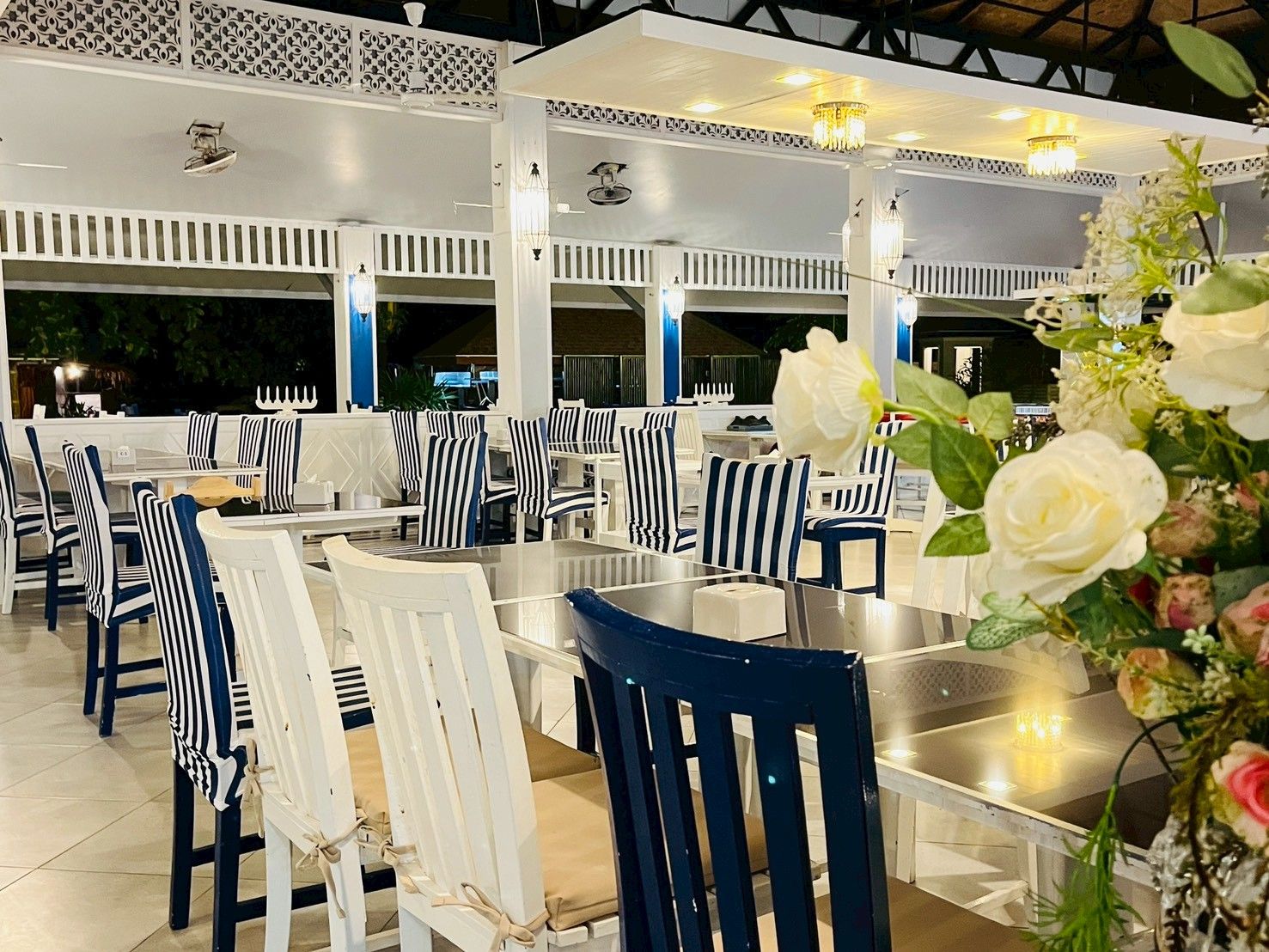 An outdoor dining area with white and blue striped chairs, round tables, and decorative lighting.