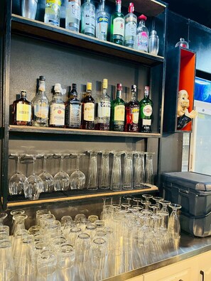 Zona de bar con estantes llenos de botellas de licores y una variedad de vasos.
