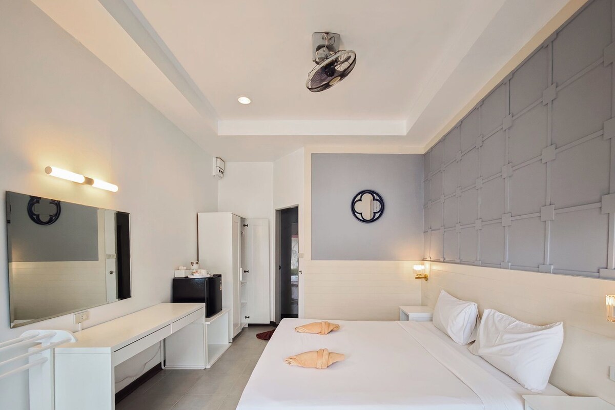 Una habitación de hotel con cama, mesitas de noche, un espejo, un armario y un ventilador de pared.