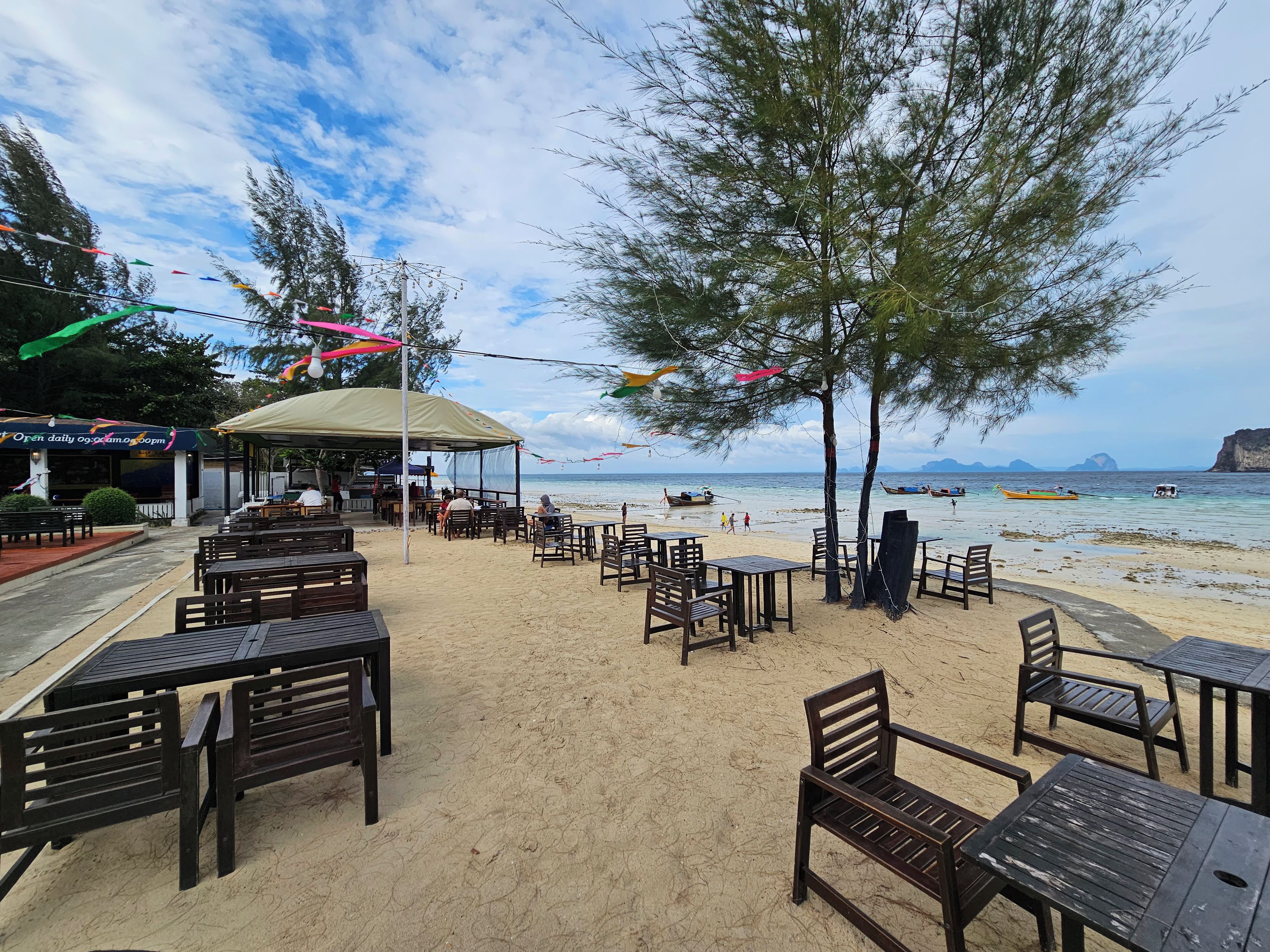 A beachside café with outdoor seating, a covered area, and a view of the sea.
