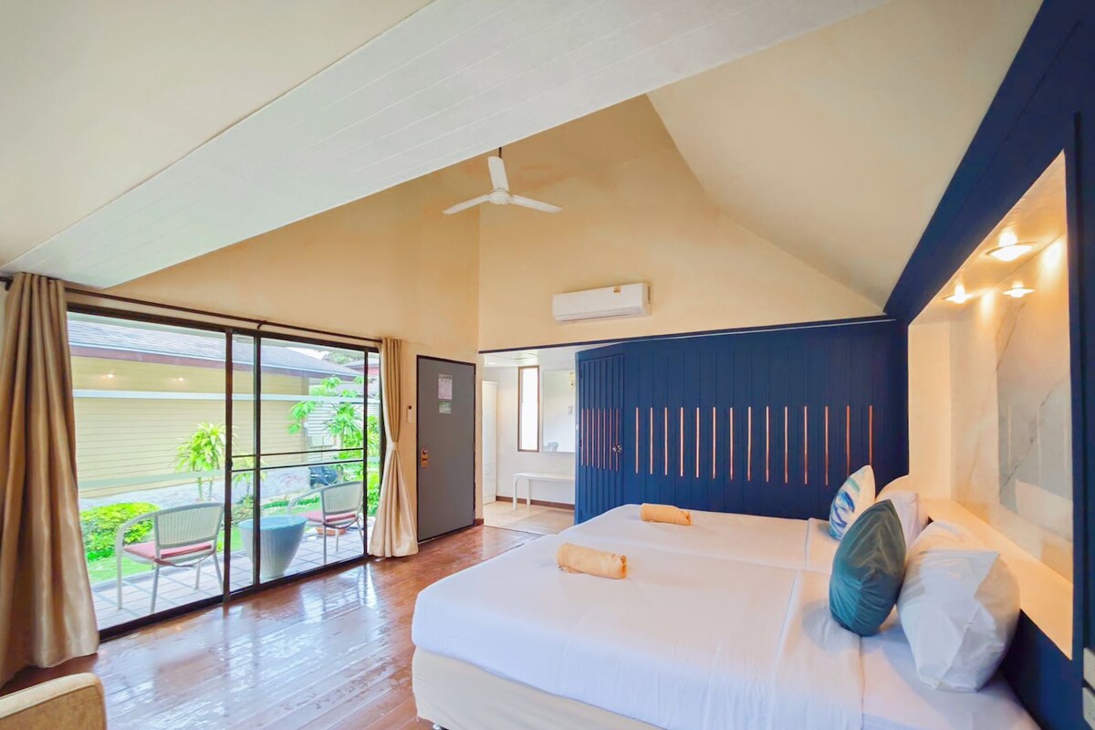 Une chambre avec un grand lit, un ventilateur de plafond et une vue sur un jardin, accessible par une porte coulissante.