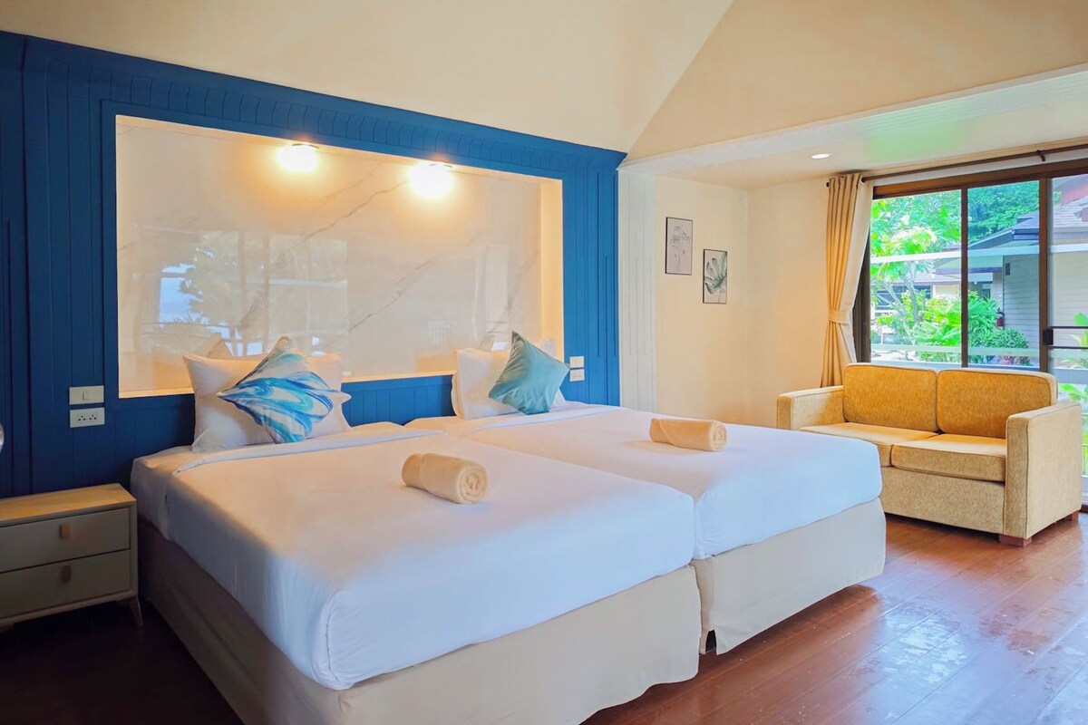 Habitación de hotel con dos camas, un sofá, un ventanal con vistas y una pared decorada en azul.