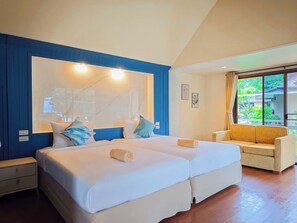 Habitació d'hotel amb dos llits, un sofà, una finestra gran amb vistes i una paret d'accent de color blau.