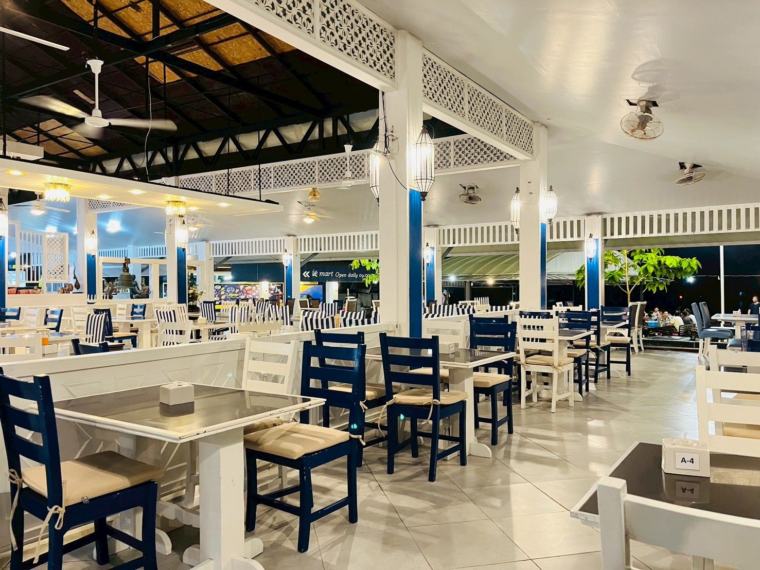 A restaurant with white and blue furniture, a high ceiling, and decorative lighting.