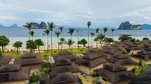Un complejo turístico costero con acceso a la playa, palmeras y edificios con techo de paja.