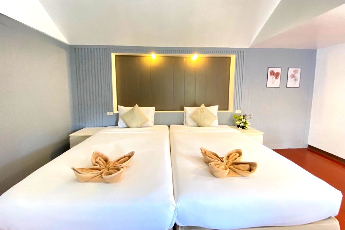 Habitación de hotel con dos camas, un espejo grande y una mesita con un florero.