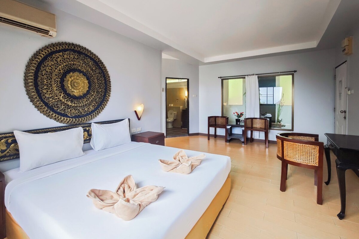 Habitación de hotel con una cama grande, un adorno en la pared, un escritorio con sillas y una ventana con cortinas.