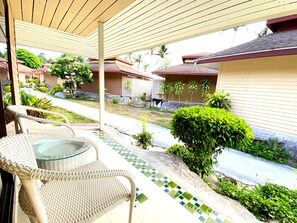 A covered outdoor area with wicker furniture, a tiled pathway, and a view of neighboring houses. - Kohhai Fantasy Resort&spa (Krabi)