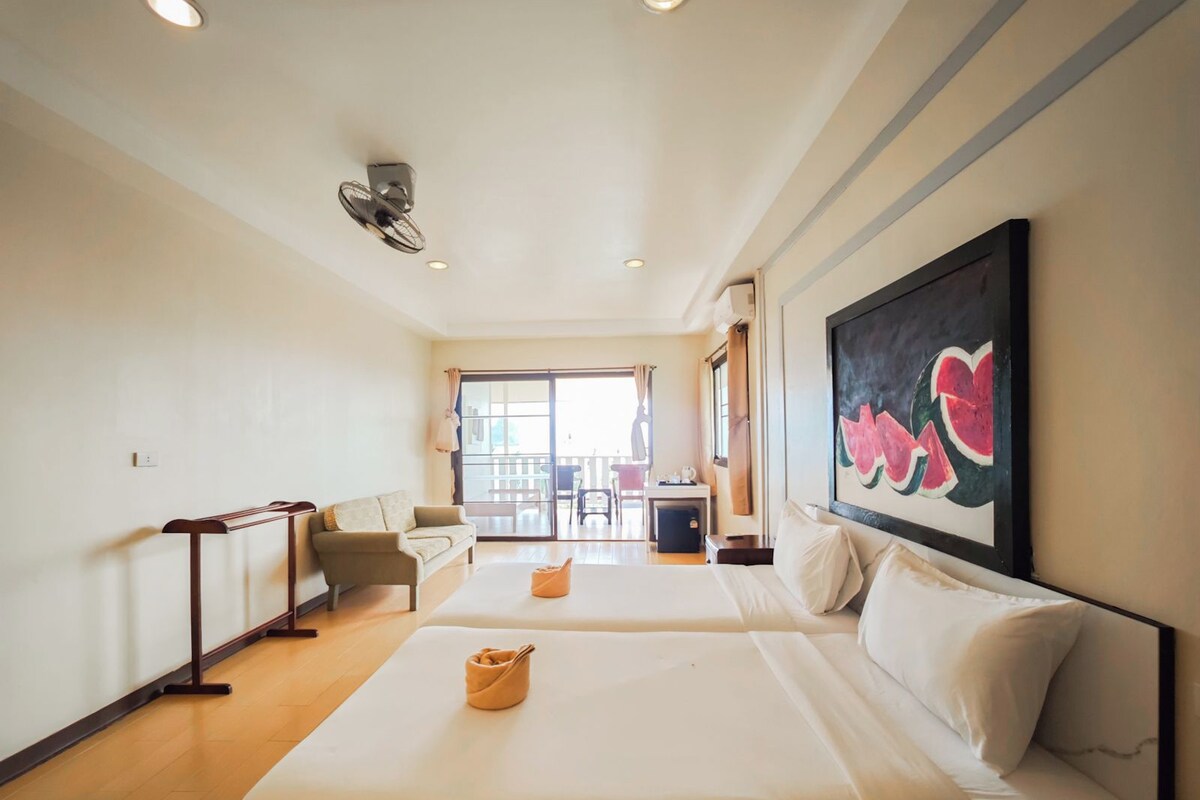 Habitación de hotel con dos camas, un escritorio, una silla, un cuadro y vistas al exterior.