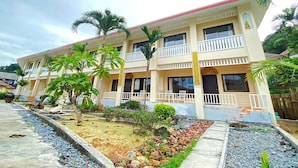 Un hôtel à plusieurs étages doté de balcons, d’un jardin agrémenté de palmiers et d’un chemin pavé.