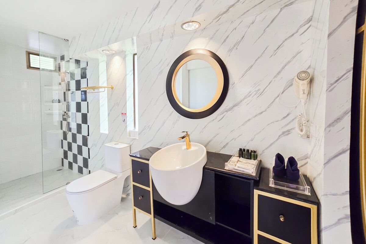 Un baño moderno con un lavamanos blanco, tocador negro y cabina de ducha de vidrio.