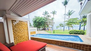 Un espace aménagé au bord de la piscine, avec un fauteuil de relaxation, une vue sur la piscine et une plage bordée de palmiers.