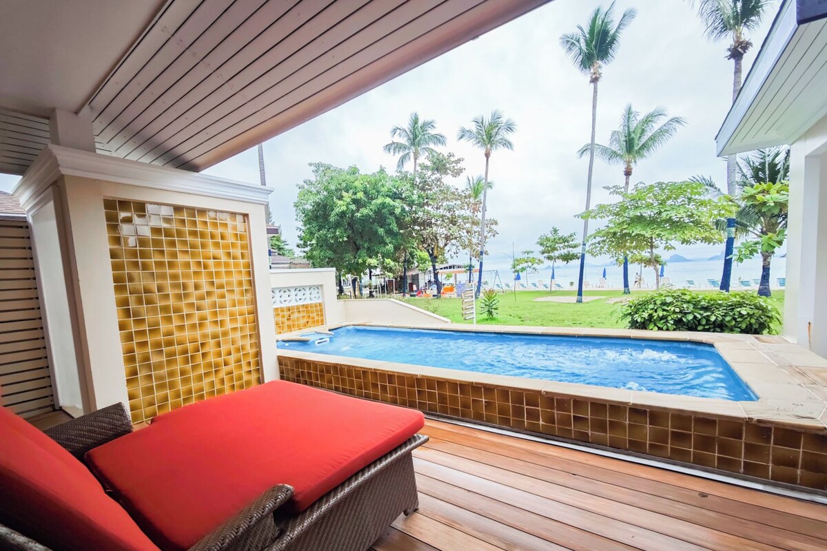 Un espace aménagé au bord de la piscine, avec un fauteuil de relaxation, une vue sur la piscine et une plage bordée de palmiers.