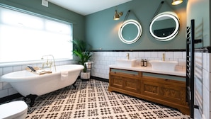 A bathroom with a freestanding bathtub, two sinks, a vanity with a mirror, and patterned floor tiles. - The Bear (Bath)