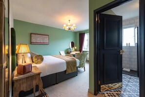 A hotel room with a bed, bedside table, lamp, and a view of the bathroom through an open door. - The Bear (Bath)