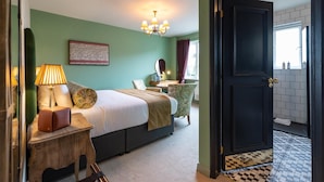 A hotel room with a bed, bedside table, lamp, and a view of the bathroom through an open door. - The Bear (Bath)