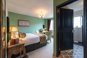 A hotel room with a bed, bedside table, lamp, and a view of the bathroom through an open door. - The Bear (Bath)