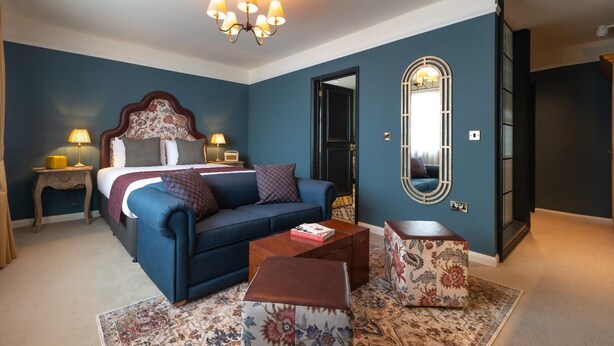 A bedroom with a bed, a sofa, a coffee table, a mirror, and a door leading to another room. - The Bear (Bath)