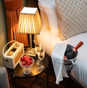 A hotel room with a bedside table featuring a radio, a bowl of strawberries, two champagne flutes, and a bottle of champagne. - The Bear (Bath)