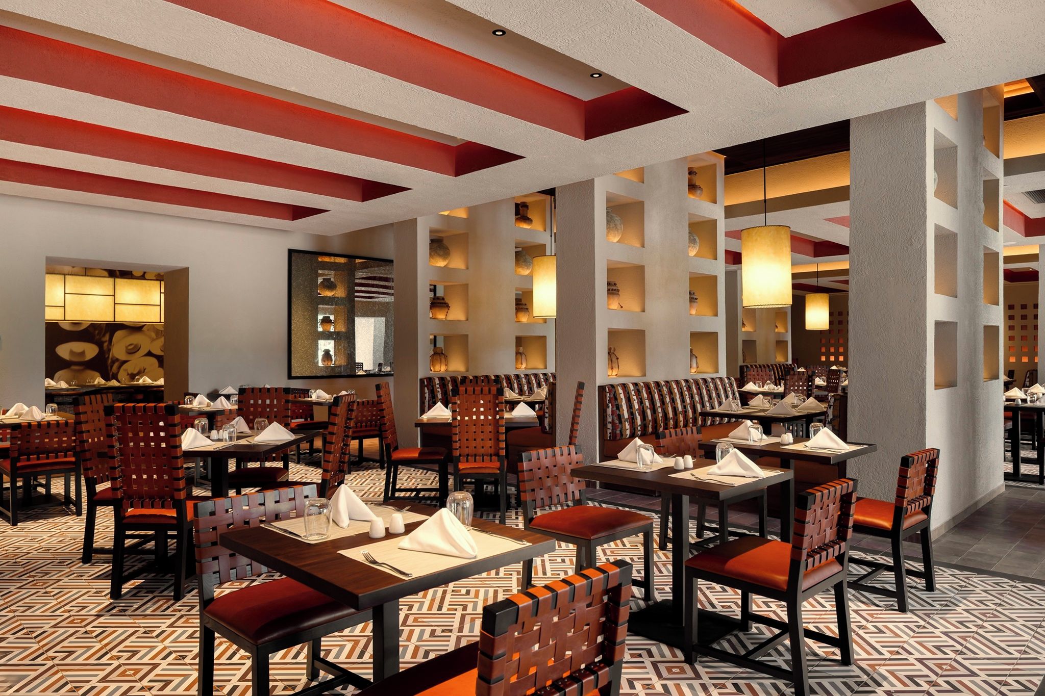 Un restaurant doté de nombreuses tables et chaises, d’un sol à motifs et d’un plafond orné de panneaux rouges et blancs.