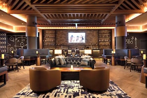 A bar area with a large screen, leather seating, and a bar stocked with bottles. - Lopesan Caoba Lagoon Resort, Spa & Casino (Punta Cana)