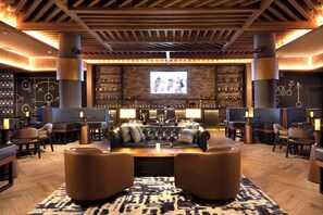 Una zona de bar con una pantalla grande, asientos de cuero y una barra llena de botellas.