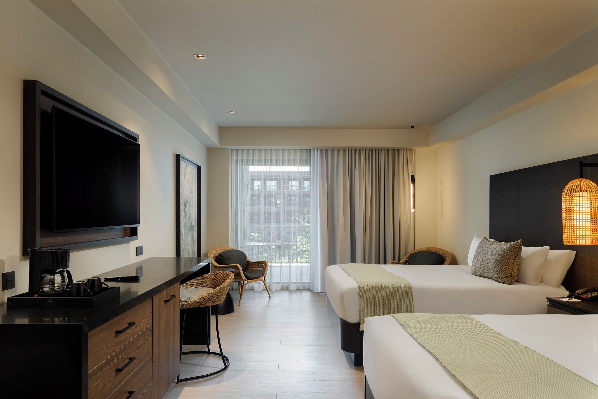 Ein Hotelzimmer mit einem Bett, einem Schreibtisch mit Fernseher, einem Sessel und einem großen Fenster mit Vorhängen.