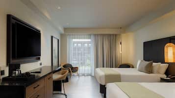 Ein Hotelzimmer mit einem Bett, einem Schreibtisch mit Fernseher, einem Sessel und einem großen Fenster mit Vorhängen.