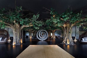 A spacious lobby with artificial trees, a central spiral sculpture, and modern seating areas. - Lopesan Caoba Lagoon Resort, Spa & Casino (Punta Cana)
