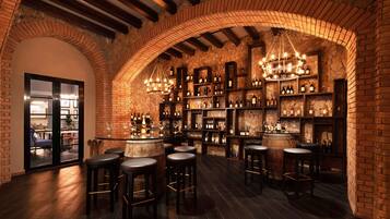 A bar area with brick walls, wooden beams, and a variety of wine bottles on shelves.