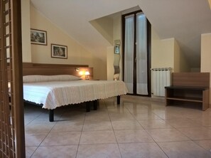 Una camera da letto con un letto matrimoniale, un comodino con una lampada, una panca in legno, una porta finestra e un termosifone.