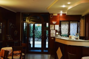 A hotel lobby with a reception desk, seating area, and a view of the street outside. - Hotel Rocco (Carugate)