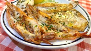Ein Teller gegrillter Meeresfrüchte mit Zitronenspalten und einer karierten Tischdecke.
