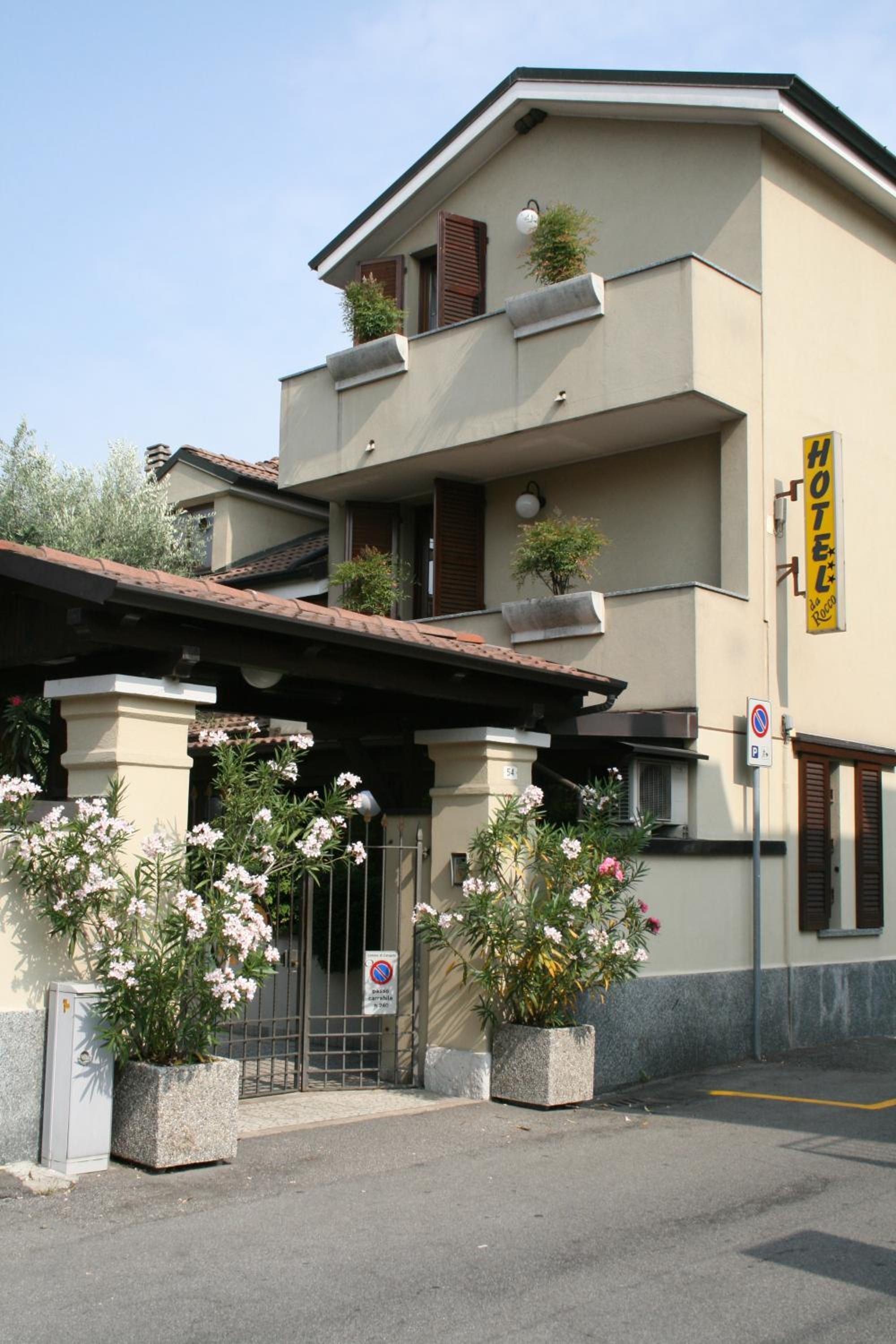A two-story building with a yellow sign indicating a hotel. There are potted plants in front of the entrance, and a no parking sign is visible.