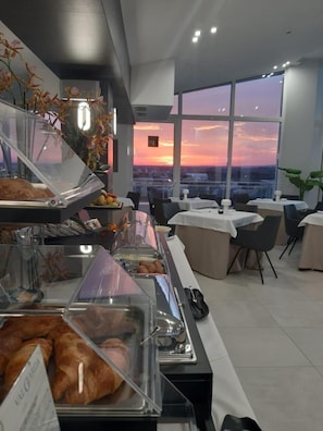 A modern breakfast buffet with clear glass containers, a city view at sunset, and contemporary furniture. - Grieco Business & Spa Hotel (Cerignola)