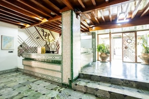 Un vestíbulo con mostrador de recepción, decoración de pared con motivos y una escalera que sube a un nivel superior.