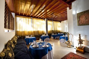 Un comedor con mesas redondas cubiertas con manteles azules, servilletas blancas y cubiertos.