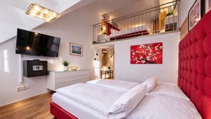 A modern bedroom with a large bed, a TV mounted on the wall, a red headboard, and a staircase leading to an upper level. - Villa Viktoria 1 - Apartments - City Center (Ingolstadt)