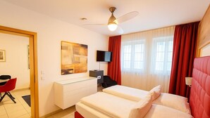 A hotel room with a bed, a desk, a chair, a television, and a ceiling fan. - Villa Viktoria 1 - Apartments - City Center (Ingolstadt)