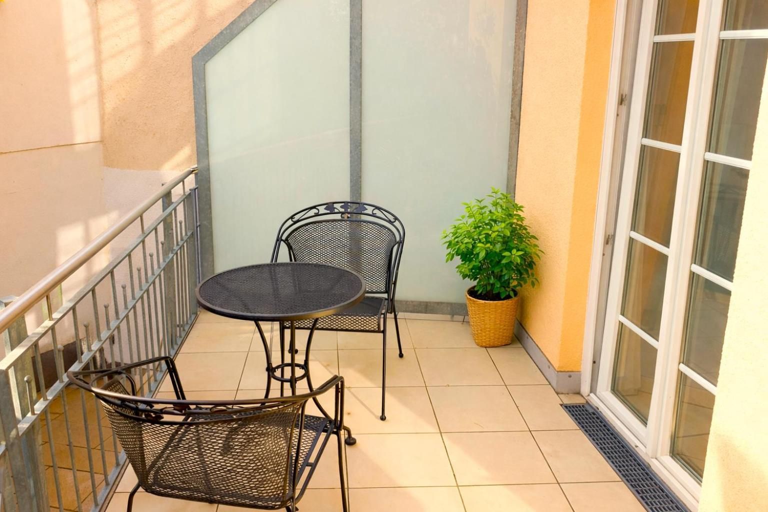 Ein kleiner Balkon mit Metalttisch und zwei Stühlen, einem Blumentopf und einer Schiebetür.
