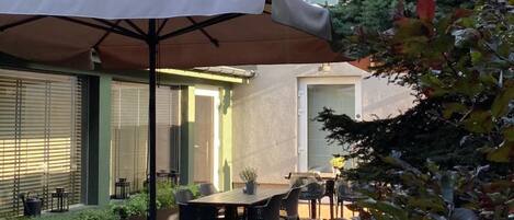 An outdoor patio area with a table and chairs, a covered seating area, and a building with air conditioning units.