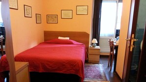 A hotel room with a bed, a desk, a chair, a nightstand, a lamp, and a window. - Affittacamere Andronaco (Milan)