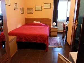 A hotel room with a bed, a desk, a chair, a nightstand, a lamp, and a window. - Affittacamere Andronaco (Milan)