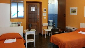 A hotel room with two beds, a desk, a chair, a television, and a bathroom visible through an open door. - Affittacamere Andronaco (Milan)