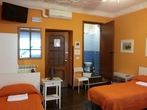 A hotel room with two beds, a desk, a chair, a television, and a bathroom visible through an open door. - Affittacamere Andronaco (Milan)